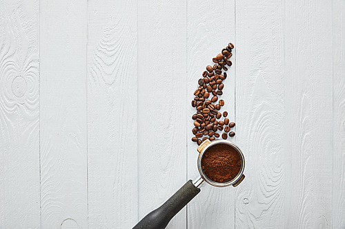 Top view of portafilter with coffee on white wooden surface with coffee beans