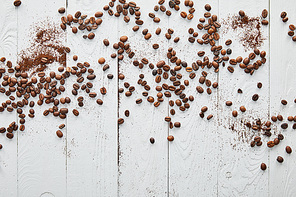 White wooden surface with scattered coffee beans and ground coffee