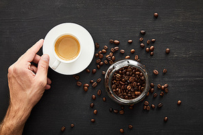 Top view of male hand with cup of coffee near glass jar with coffee beans