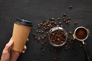 Top view of hand with paper cup under dark wooden surface with glass jar and portafilter