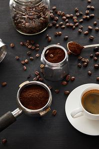 Geyser coffee maker near cup of coffee, portafilter, spoon and glass jar on dark wooden surface with coffee beans