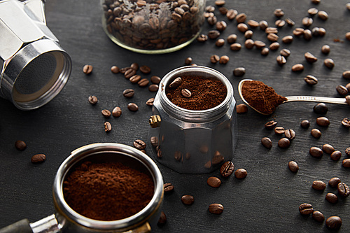 Parts of geyser coffee maker near spoon with coffee and portafilter on dark wooden surface with coffee beans