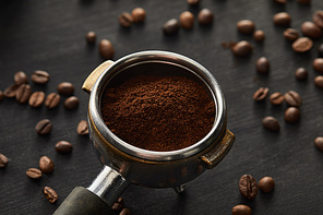 Portafilter filled with fresh coffee on dark wooden surface with coffee beans