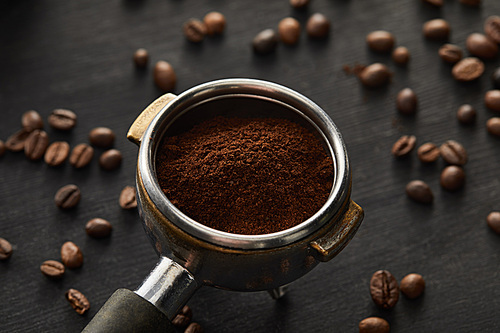 Portafilter filled with fresh coffee on dark wooden surface with coffee beans