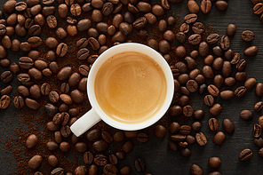 Top view of white cup with espresso on dark surface with scattered coffee beans