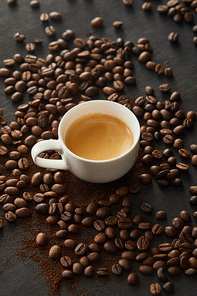 White cup with coffee on dark surface with scattered coffee beans