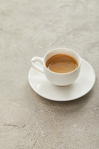 White cup with coffee on saucer on light marble surface