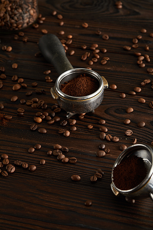Portafilters with ground coffee on dark wooden surface with coffee beans