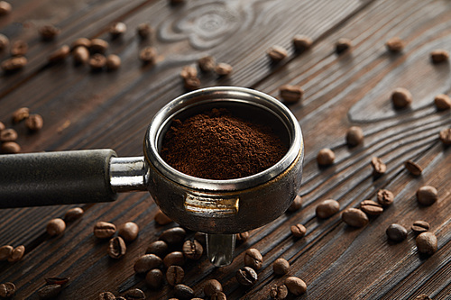 Portafilter filled with fresh ground coffee on dark wooden surface with coffee beans