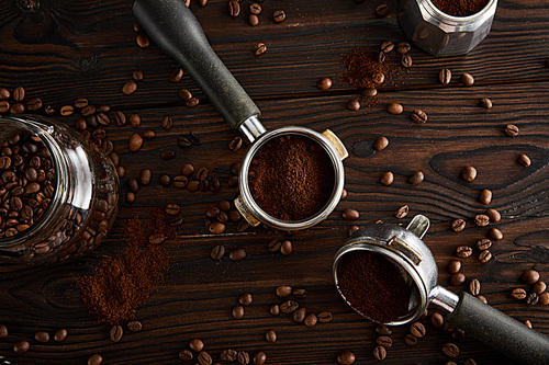 Portafilters between glass jar and geyser coffee maker on dark wooden surface