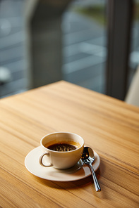 selective focus of cup with coffee near spoon on wooden table in cafe
