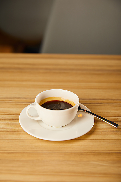 white cup with coffee near spoon in cafe