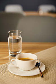 selective focus of cup with hot coffee near glass with water in cafe