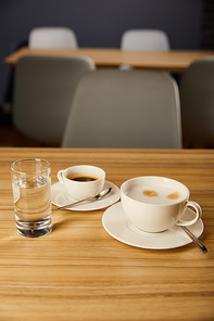 selective focus of cups with coffee near glass of water in cafe