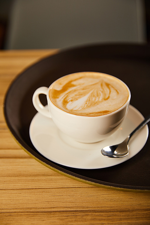 selective focus of cappuccino in white cup with saucer on black tray