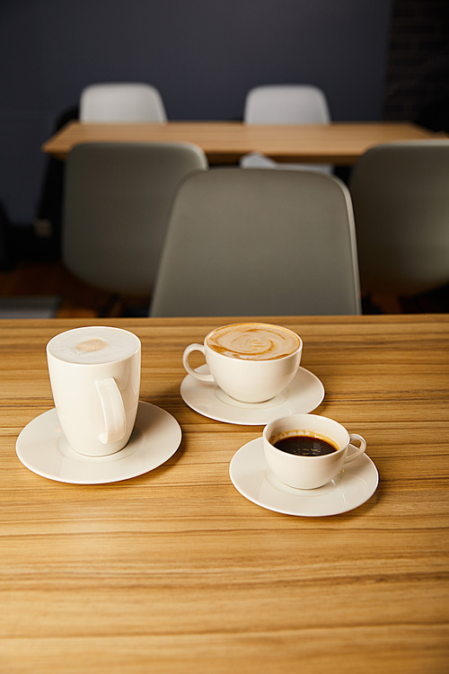 selective focus of tasty coffee in white cups on wooden table