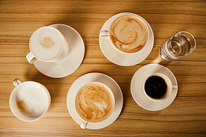 top view of saucers with cups of different coffee near glass of water