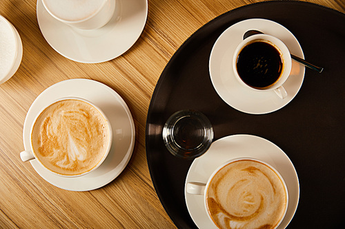top view of cups of different coffee near glass of water on tray
