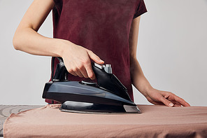 Cropped view of woman with black iron ironing shirt isolated on grey