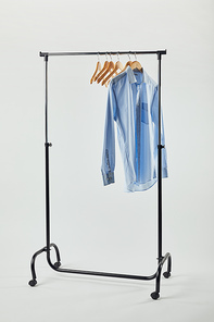 Straight rack, wooden hangers and blue shirt isolated on grey