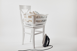 White chair, laundry basket with clothes and iron on grey
