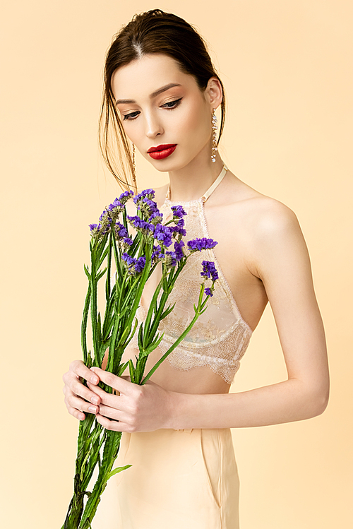 attractive woman looking at purple limonium flowers isolated on beige
