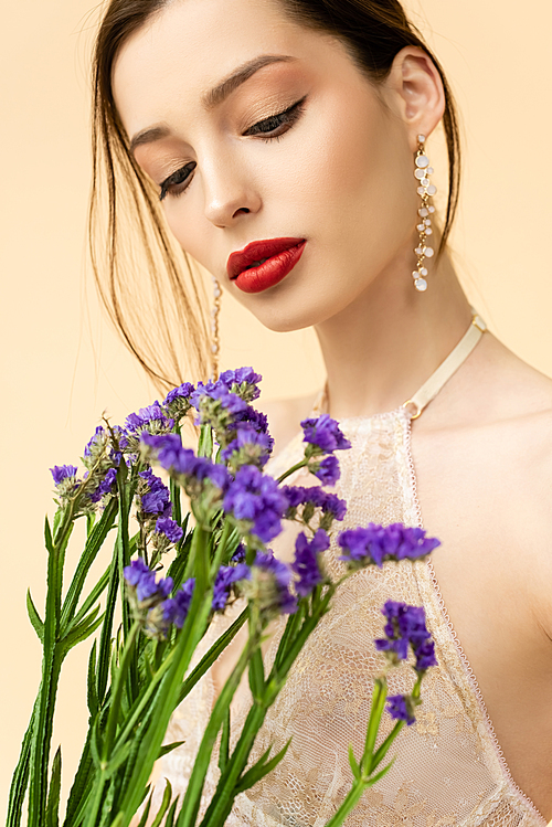 young and attractive woman holding purple limonium flowers isolated on beige