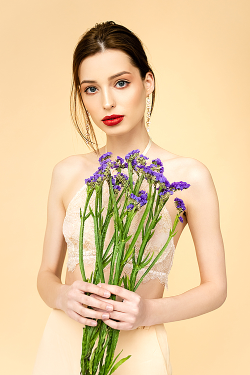 young woman holding purple limonium flowers isolated on beige
