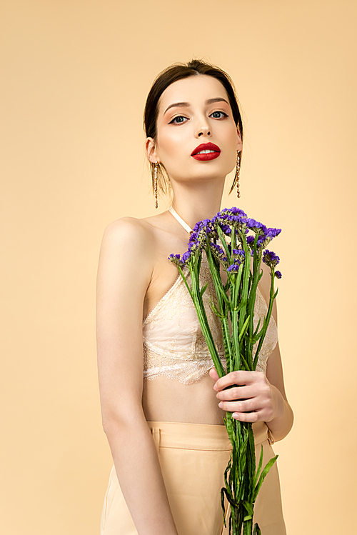young and attractive woman holding limonium flowers isolated on beige