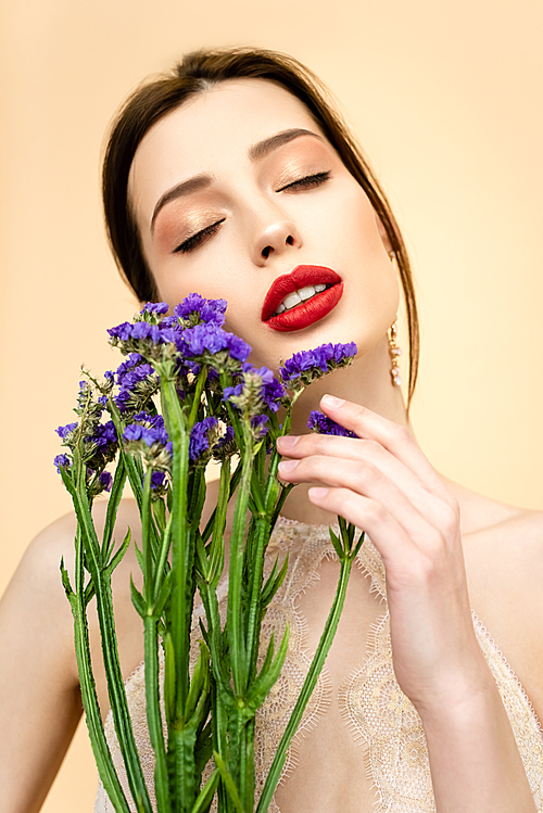 pretty woman with closed eyes holding purple limonium flowers isolated on beige