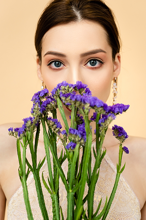 young attractive woman covering face with purple limonium flowers isolated on beige