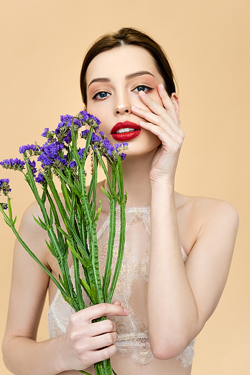 beautiful woman  and touching face while holding limonium flowers isolated on beige