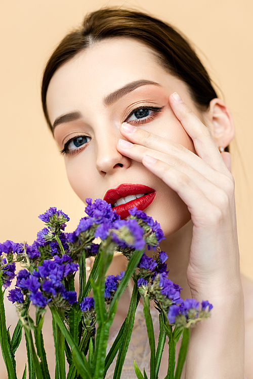 beautiful woman  and touching face near purple flowers isolated on beige