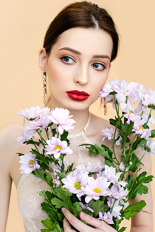 young woman holding blooming chrysantemum flowers and looking away isolated on beige