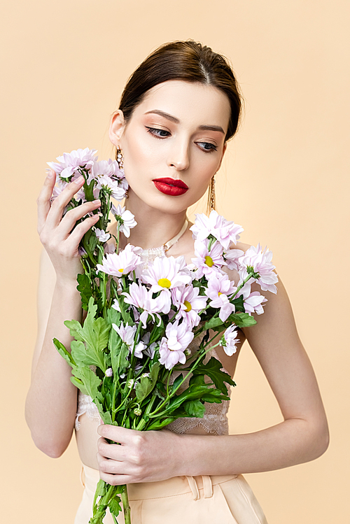 pretty young woman looking away near blooming chrysanthemum flowers isolated on beige