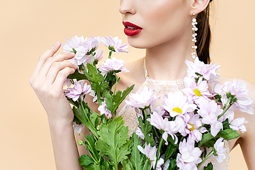 cropped view of young woman holding blooming flowers isolated on beige