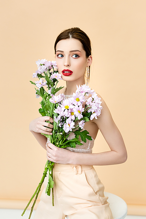 pretty woman looking away and holding blooming chrysanthemum flowers on beige
