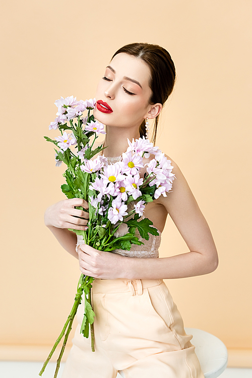 pretty woman with closed eyes holding blooming chrysanthemum flowers on beige