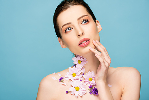 naked young woman with flowers on neck touch face isolated on blue