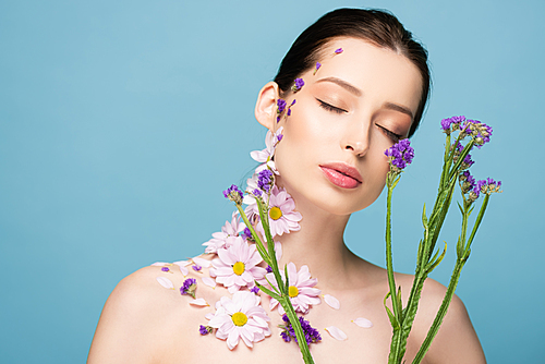 naked young woman with closed eyes near blooming flowers isolated on blue