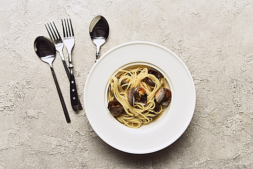 top view of delicious pasta with mollusks near cutlery on textured white background