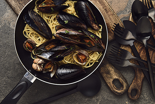 top view of delicious pasta with mollusks and mussels in frying pan on weathered grey background