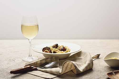 Italian pasta with seafood served with white wine, napkin and cutlery isolated on grey