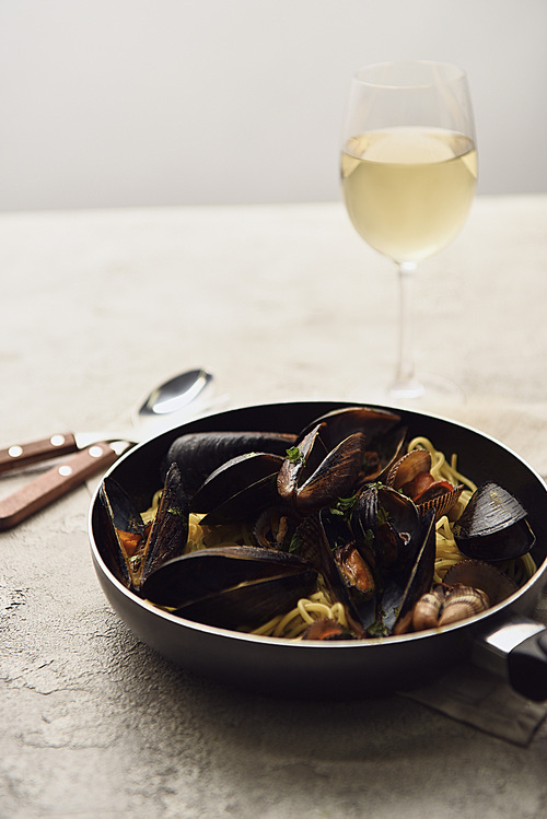 selective focus of delicious Italian pasta with seafood served in frying pan with white wine isolated on grey