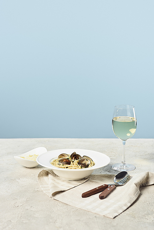 delicious Italian spaghetti with seafood served with white wine on napkin near cutlery isolated on blue