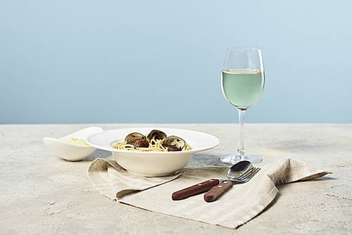 delicious Italian spaghetti with seafood served with grated cheese and white wine on napkin near cutlery isolated on blue