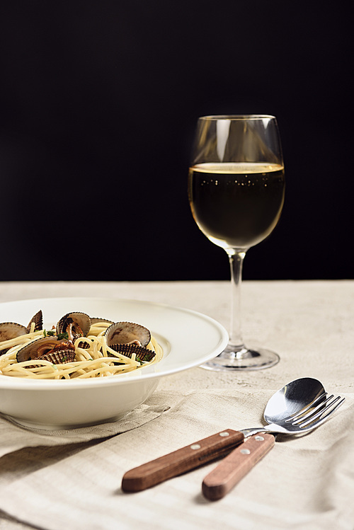 delicious Italian spaghetti with seafood served with white wine on napkin near cutlery isolated on black