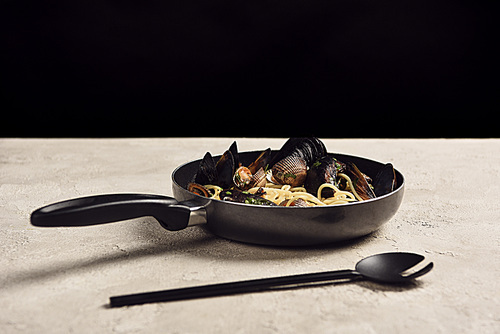 delicious Italian pasta with seafood served in frying pan near spatula isolated on black