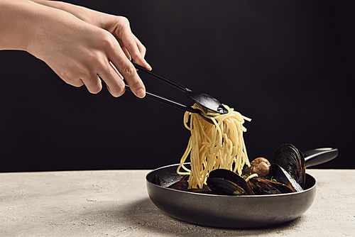 cropped view of woman taking tasty Italian spaghetti with seafood from frying pan isolated on black