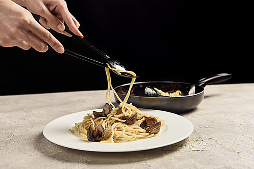 partial view of woman putting delicious Italian spaghetti with seafood on plate isolated on black